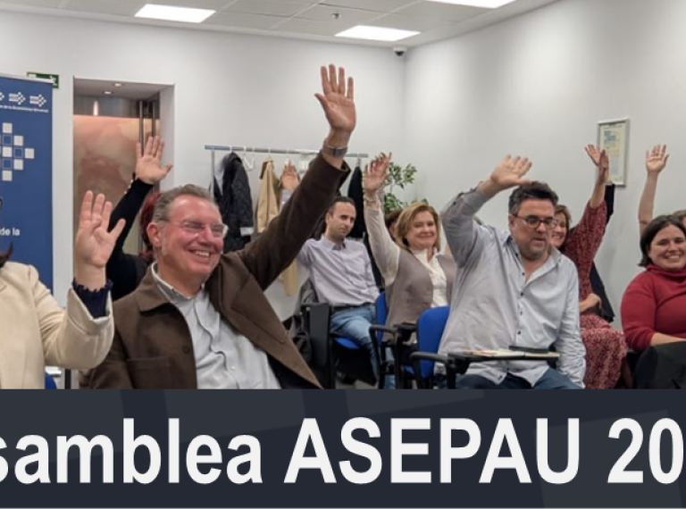 grupo de personas sentadas en una sala en varias filas con una mano levantada y sonriendo